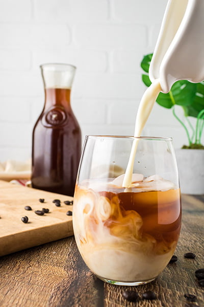 Person pouring milk on iced coffee Person pouring milk on iced coffee