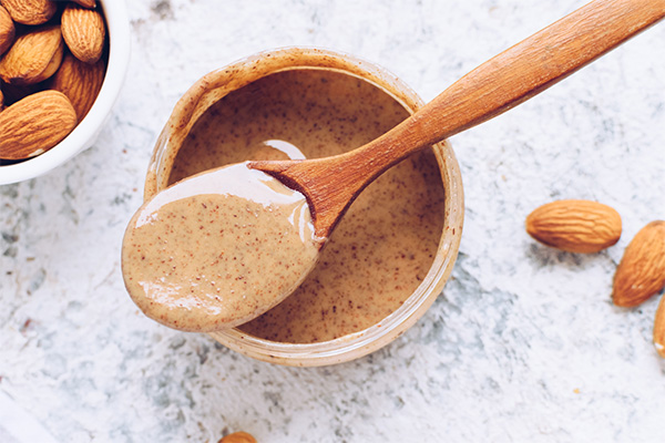 Almond nut butter in bowl with wooden spoon, almonds on side