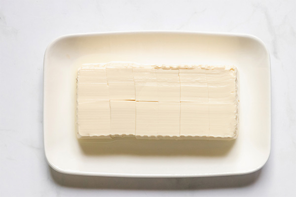 Block of tofu scored on a white rectangular dish