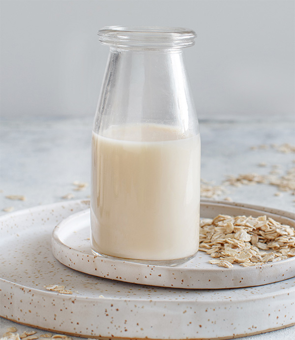 Oat milk bottle on plate with oats on a gray background