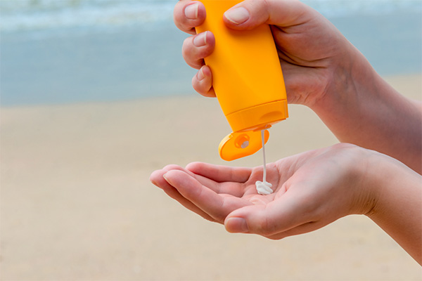 Person applying sunscreen from an orange bottle