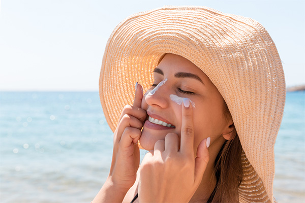 Woman wearing a hat applying sunscreen